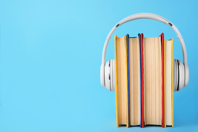 Books and modern headphones on light blue background. Space for text