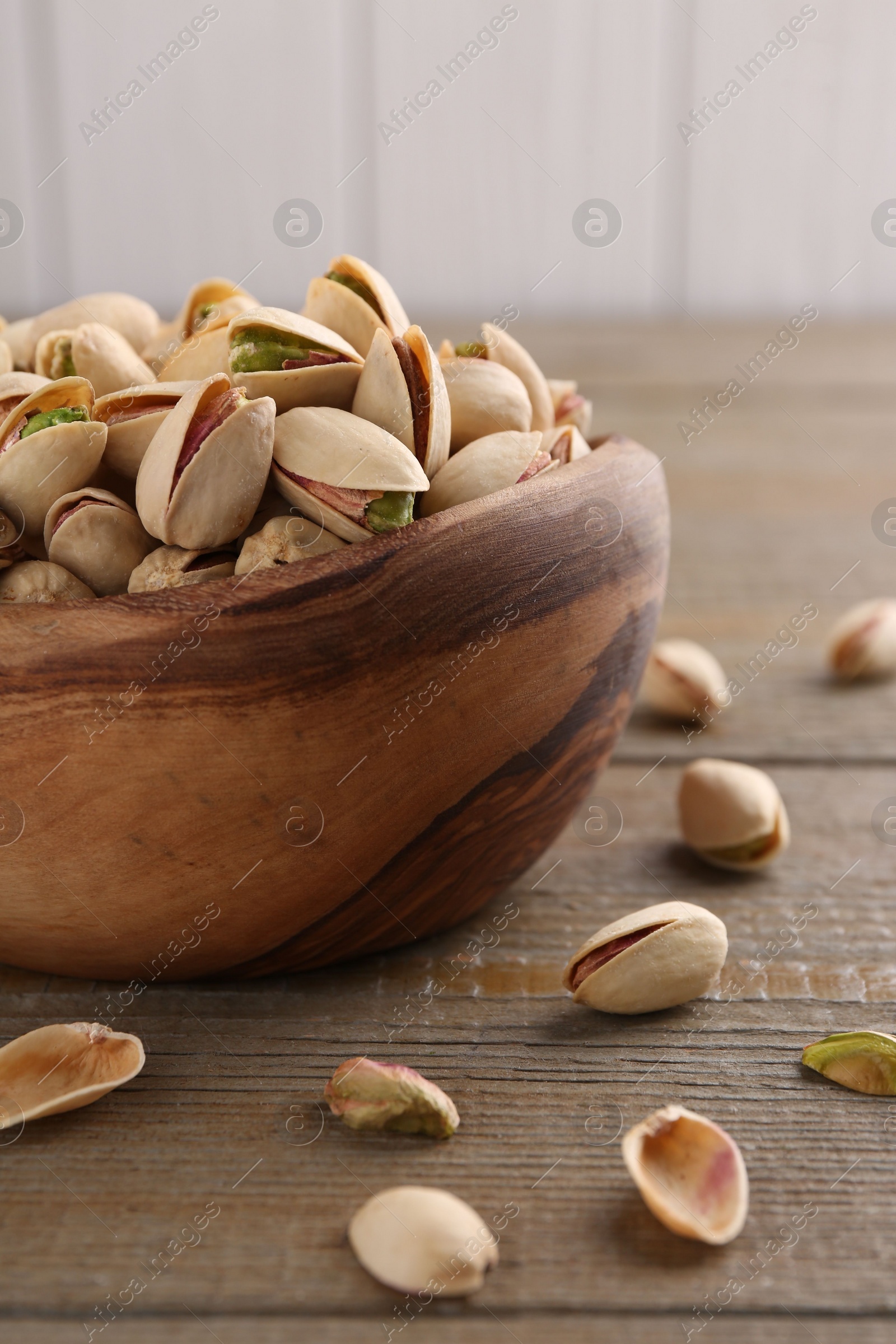 Photo of Tasty pistachios in bowl on wooden table, closeup