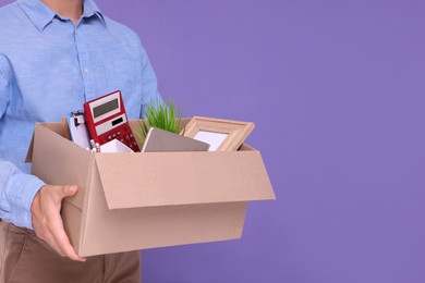 Photo of Unemployed man with box of personal office belongings on purple background, closeup. Space for text