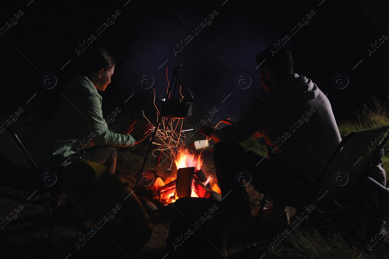 Photo of Couple warming hands near bonfire outdoors at night. Camping season