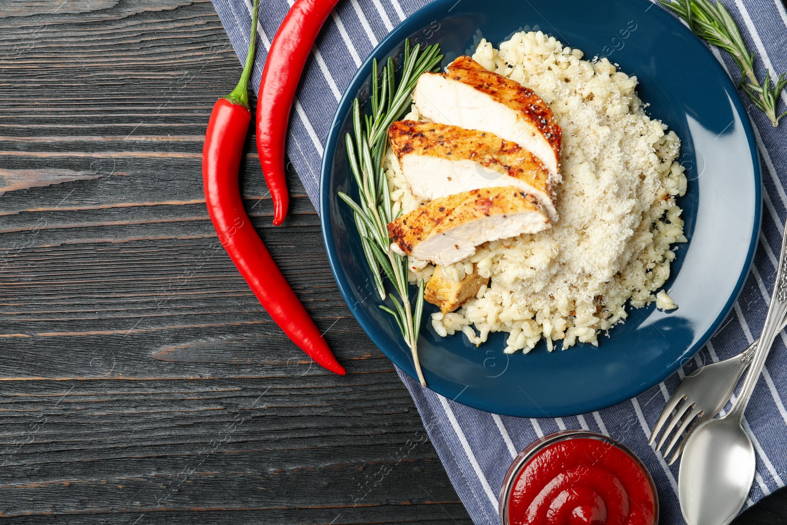 Photo of Delicious chicken risotto served on black wooden table, flat lay