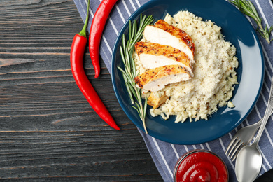 Photo of Delicious chicken risotto served on black wooden table, flat lay