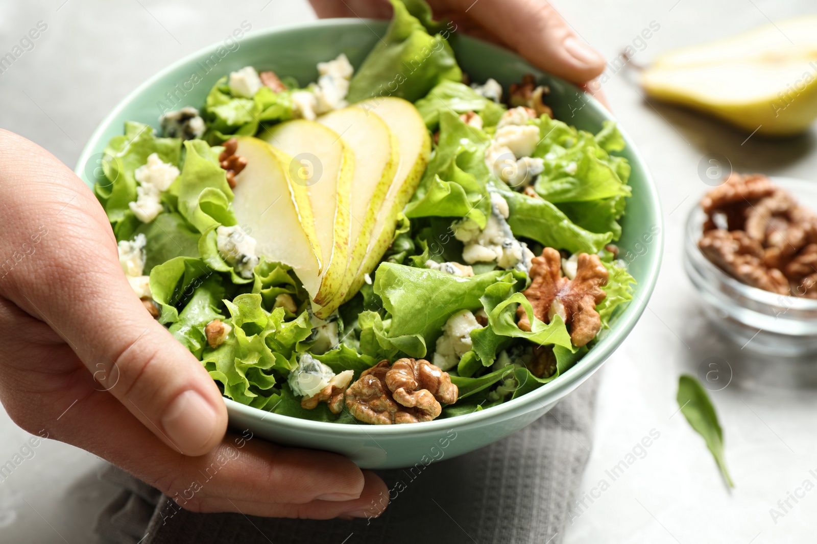 Photo of Woman holding tasty salad with pear slices at table, closeup