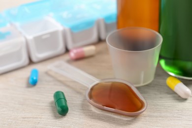 Dosing spoon with syrup, measuring cup and pills on wooden table, closeup. Cold medicine