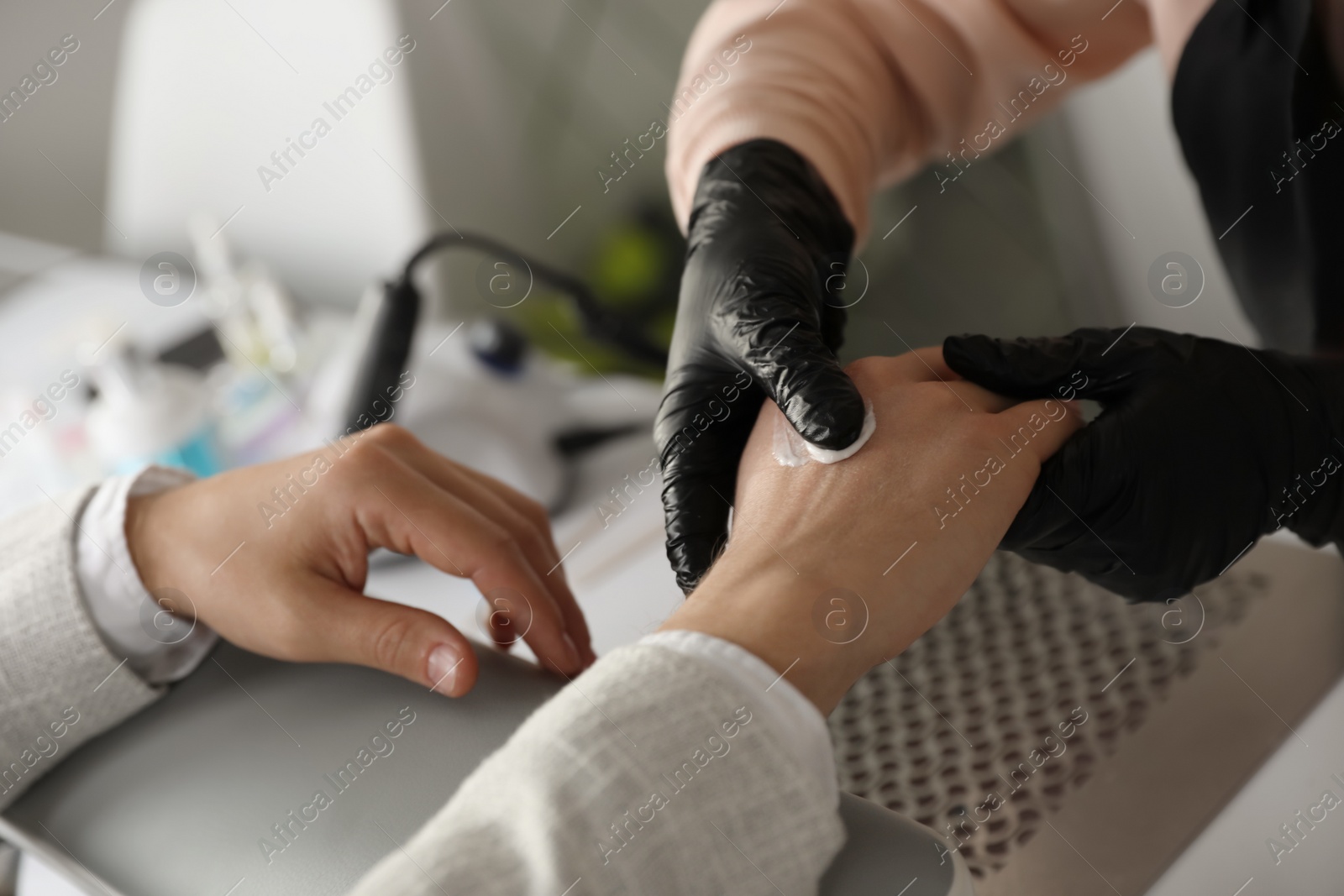 Photo of Professional manicurist applying cream on client's hand in beauty salon, closeup