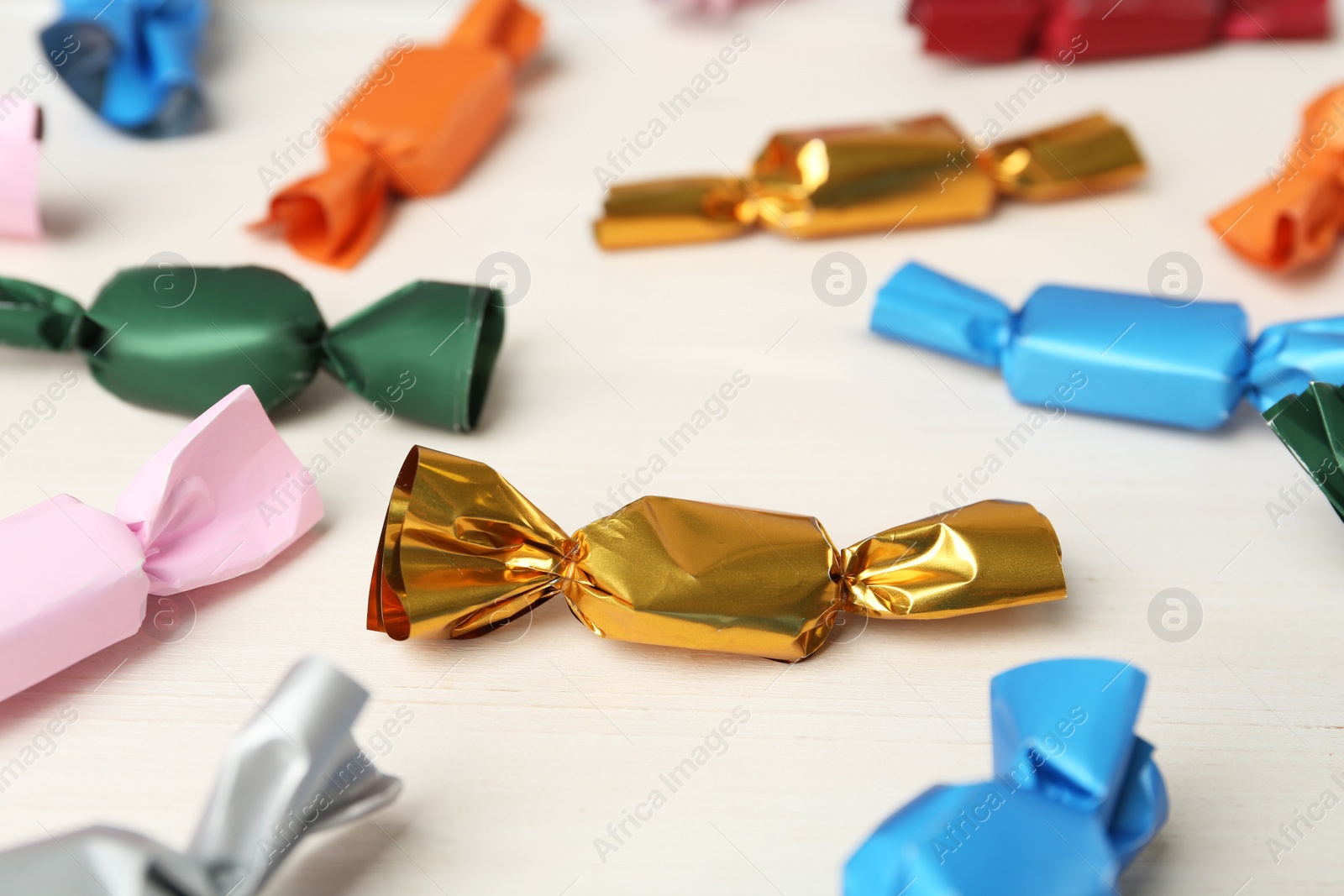 Photo of Candies in colorful wrappers on white wooden table, closeup