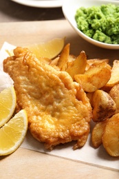 Photo of British traditional fish and potato chips on wooden board, closeup