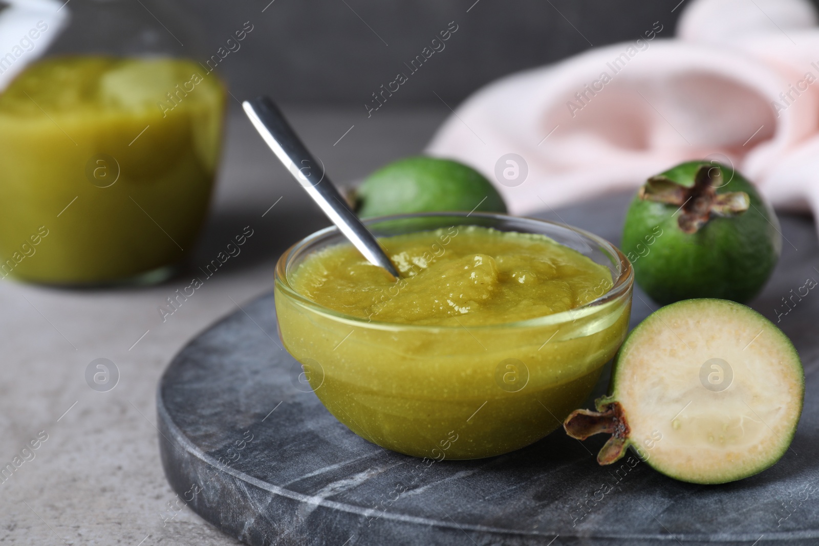Photo of Feijoa jam and fresh fruits on grey table, closeup