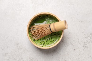Photo of Bowl of fresh matcha tea with bamboo whisk on light table, top view