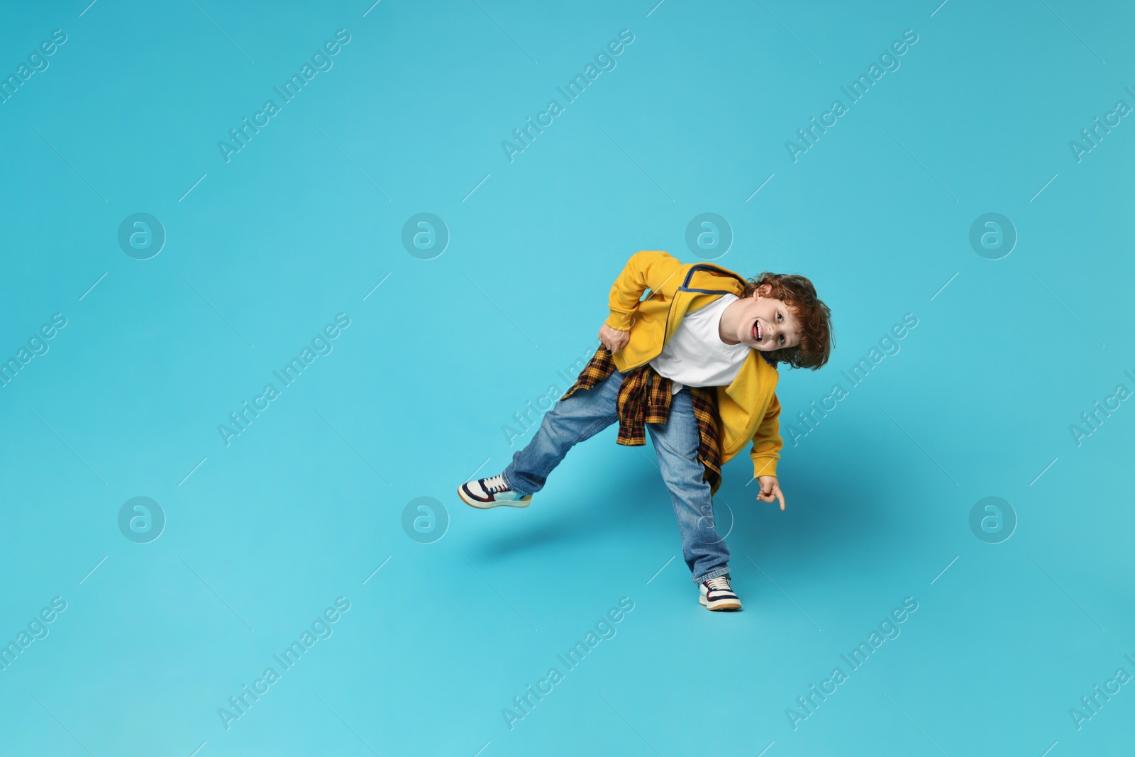 Photo of Happy little boy dancing on light blue background. Space for text