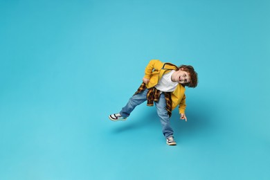 Happy little boy dancing on light blue background. Space for text