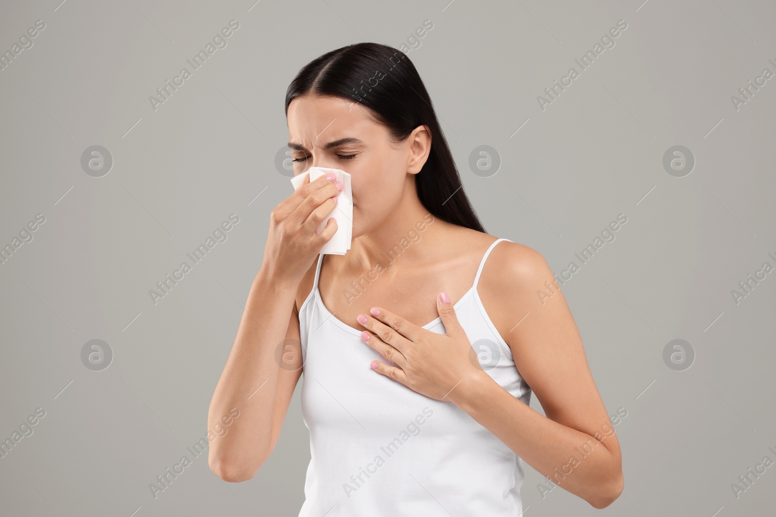 Photo of Suffering from allergy. Young woman blowing her nose in tissue on light grey background