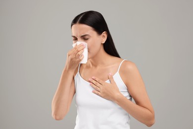 Photo of Suffering from allergy. Young woman blowing her nose in tissue on light grey background