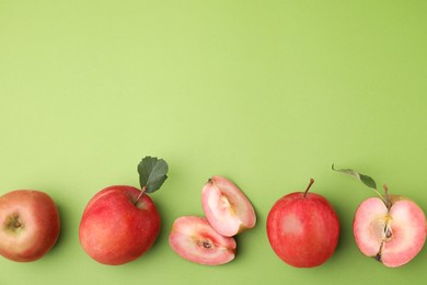 Photo of Tasty apples with red pulp and leaves on light green background, flat lay. Space for text