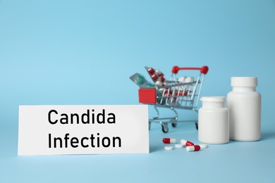Card with phrase Candida Infection and pills on light blue background