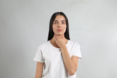 Young woman doing thyroid self examination on light background