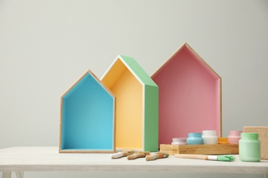 House shaped shelves, jars of paints and brushes on white table. Interior elements