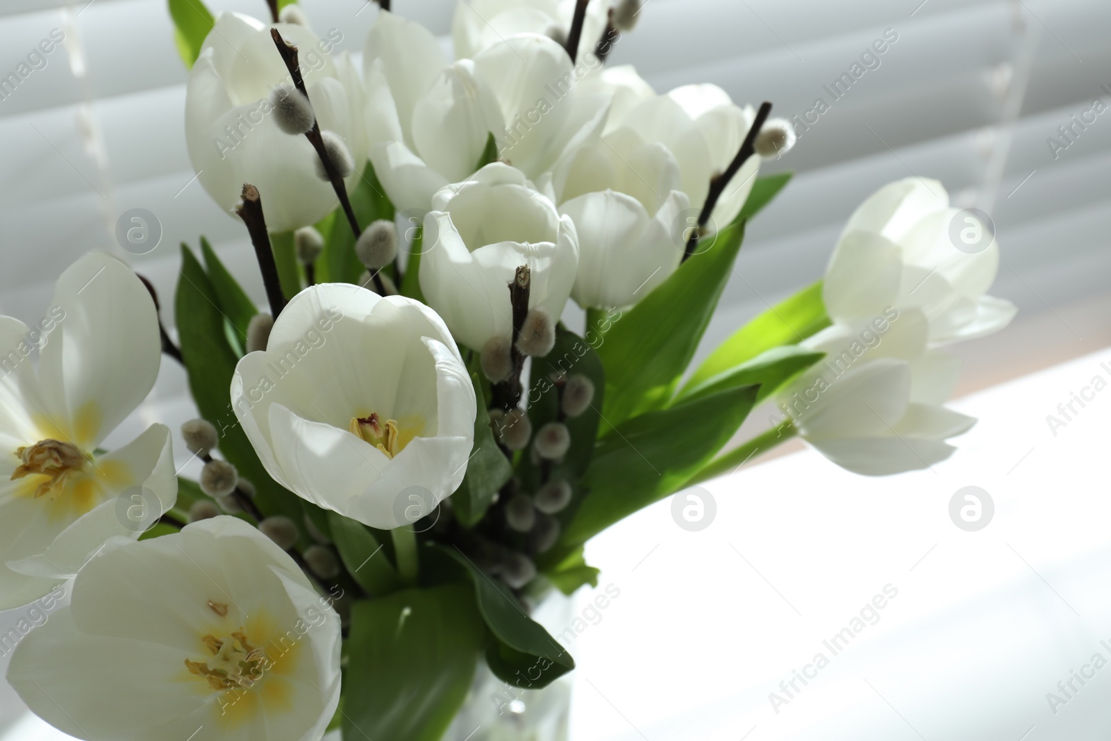 Photo of Beautiful bouquet of willow branches and tulips near window, closeup. Space for text