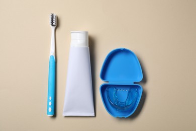 Toothpaste, brush and container with dental mouth guard on beige background, flat lay. Bite correction