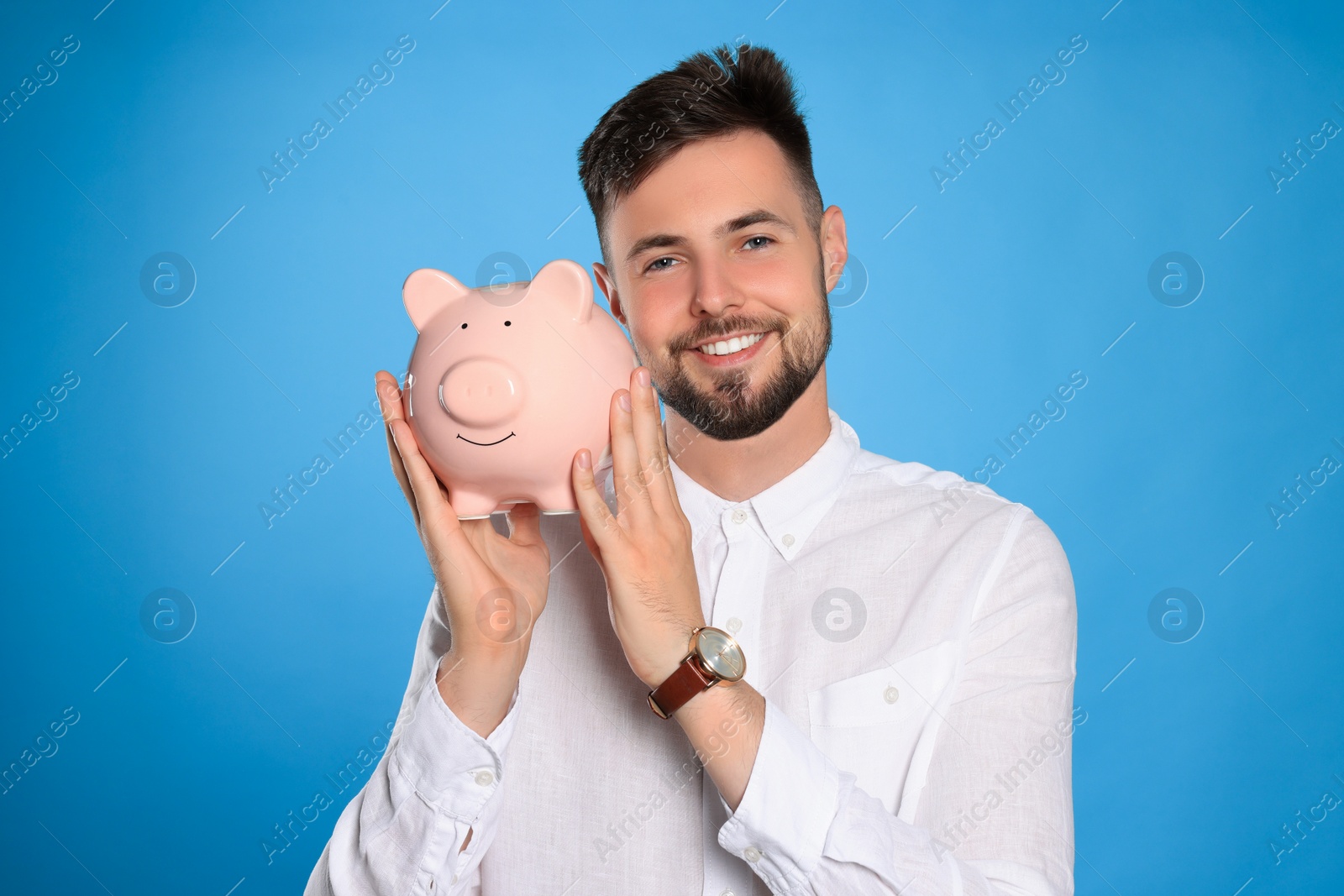 Photo of Happy young man with piggy bank on light blue background