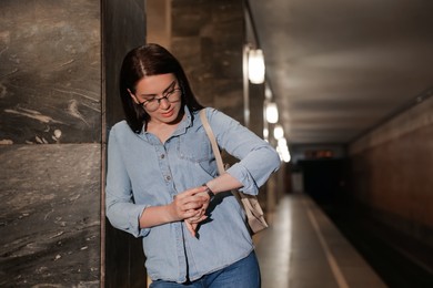 Beautiful woman with backpack looking at wristwatch on subway station. Public transport
