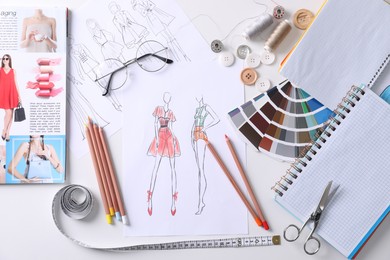 Photo of Sketches of clothes and different stuff on white table, flat lay. Fashion designer's workplace