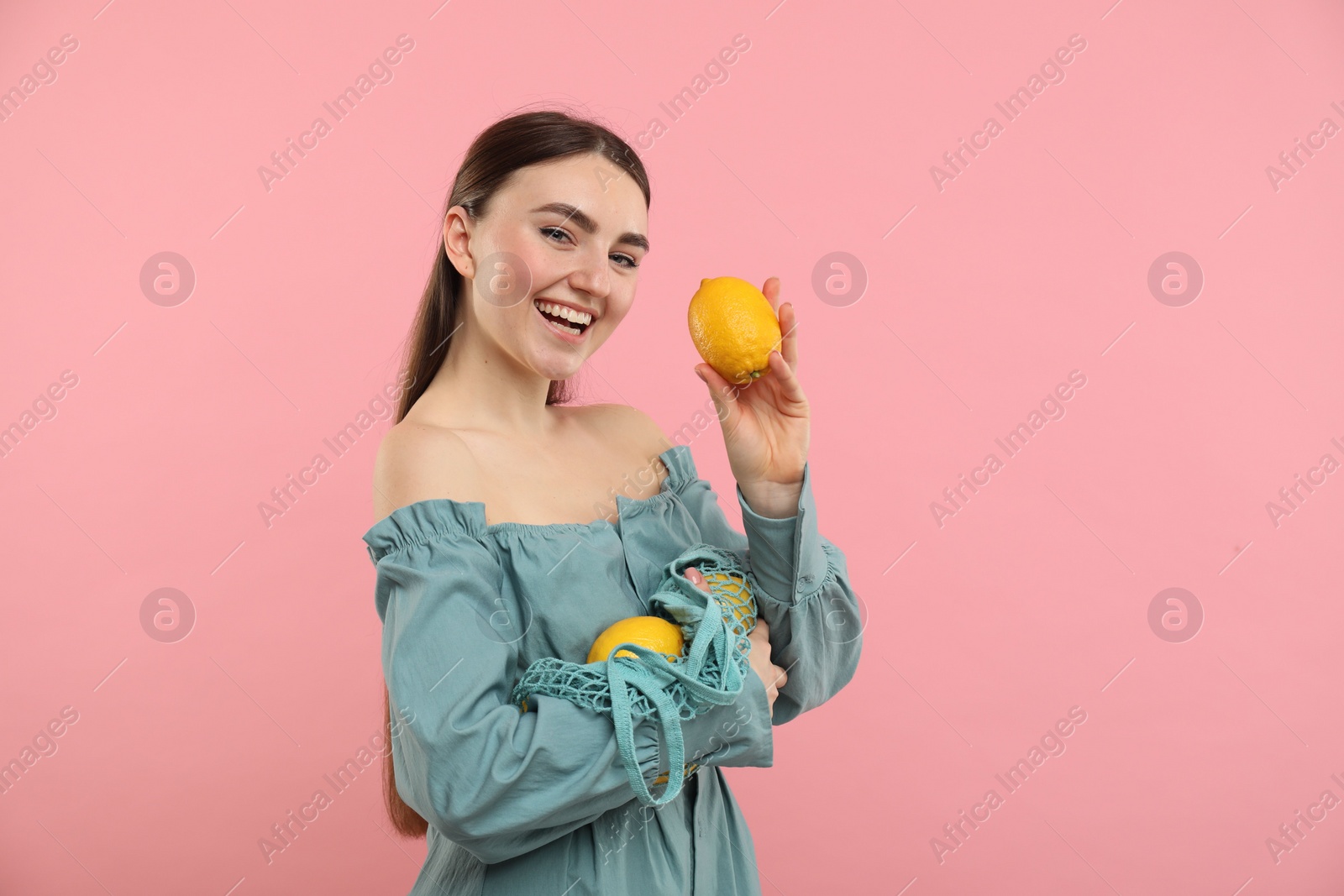 Photo of Woman with string bag of fresh lemons on pink background, space for text