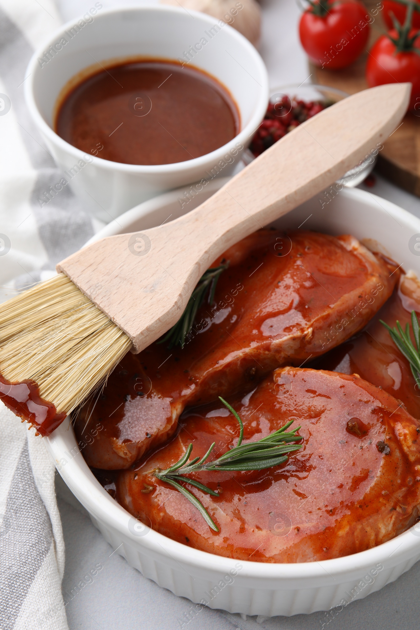 Photo of Raw marinated meat, rosemary and basting brush on table, closeup