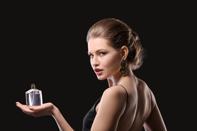 Beautiful young woman with bottle of perfume on black background