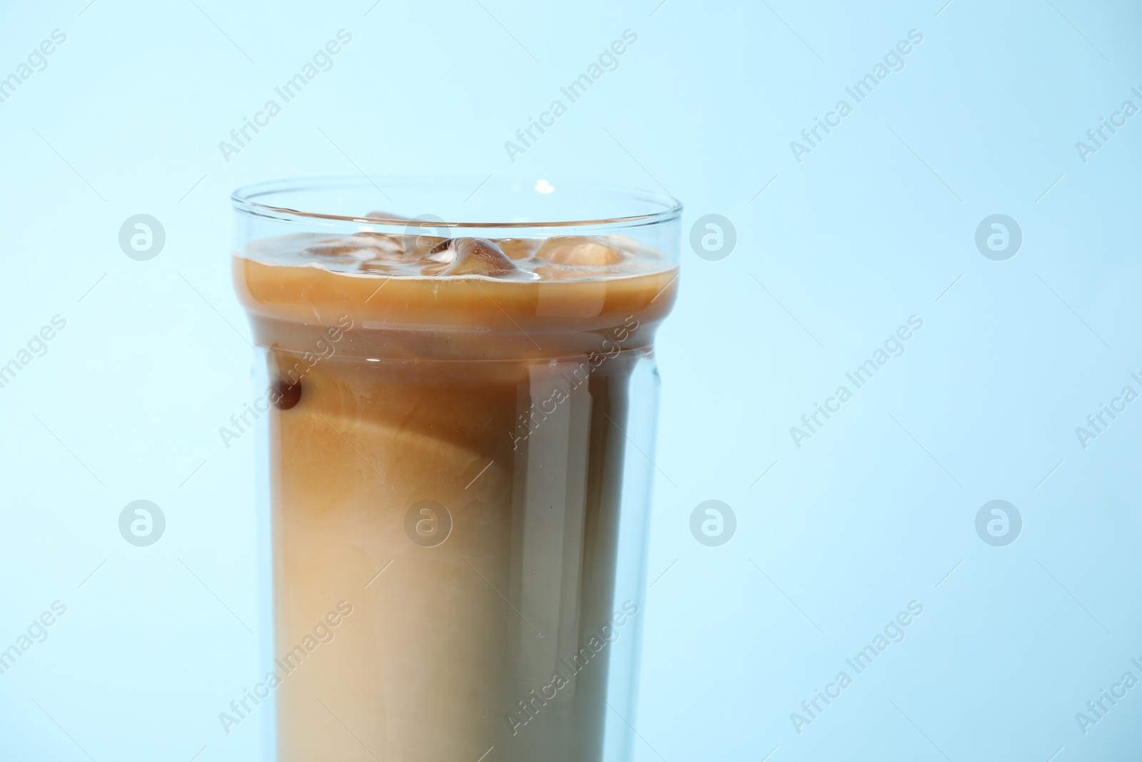 Photo of Glass of iced coffee on light blue background, closeup. Space for text