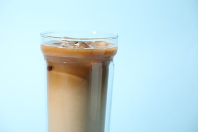 Photo of Glass of iced coffee on light blue background, closeup. Space for text