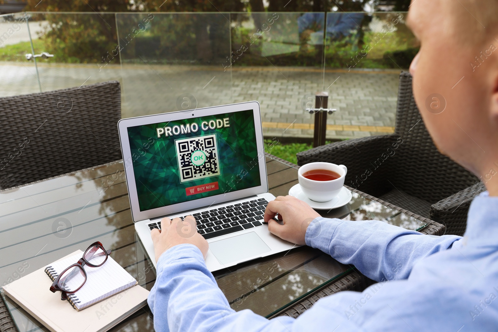 Photo of Man with laptop activating promo code at wooden table outdoors, closeup