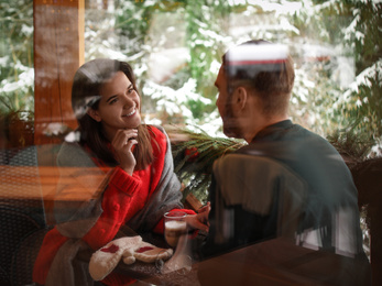 Lovely couple at table in cafe, view through window. Winter vacation