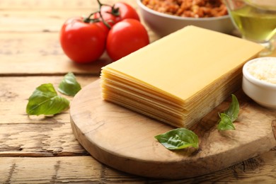 Cooking lasagna. Board with pasta sheets and other products on wooden table, closeup. Space for text