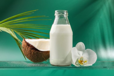 Photo of Bottle of delicious vegan milk, coconut, palm leaf and flower on green background