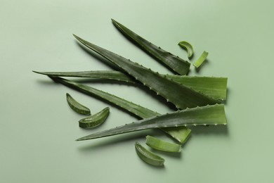 Photo of Cut aloe vera leaves on light green background, flat lay