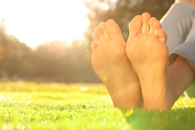 Photo of Young woman sitting barefoot on fresh green grass outdoors, closeup