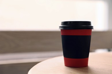 Photo of Hot coffee in takeaway paper cup on wooden table at cafe, space for text