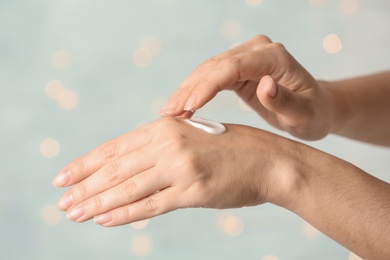 Photo of Woman applying hand cream on blurred background, closeup