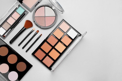 Colorful contouring palettes and brushes on light grey background, flat lay with space for text. Professional cosmetic product
