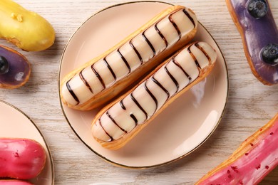 Photo of Different tasty glazed eclairs on light wooden table, flat lay