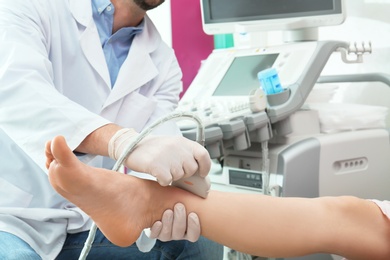 Doctor conducting ultrasound examination of patient's leg in clinic, closeup