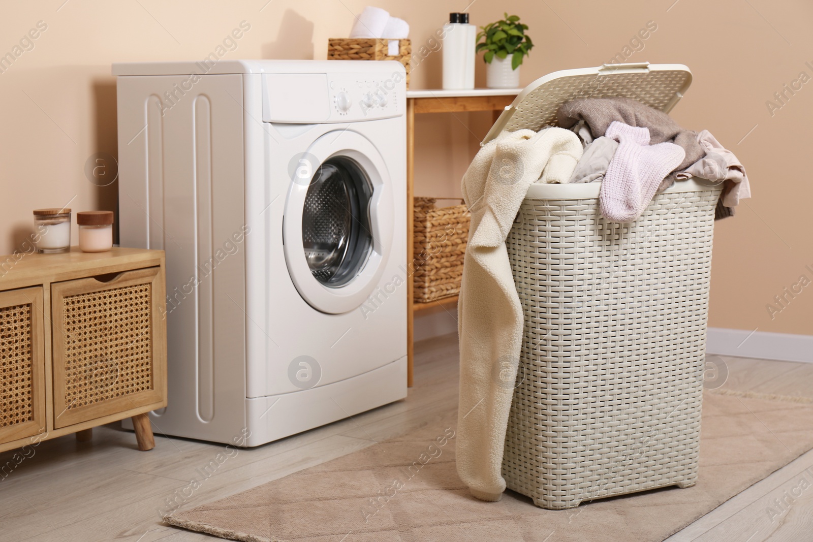 Photo of Laundry basket overfilled with clothes near washing machine in bathroom