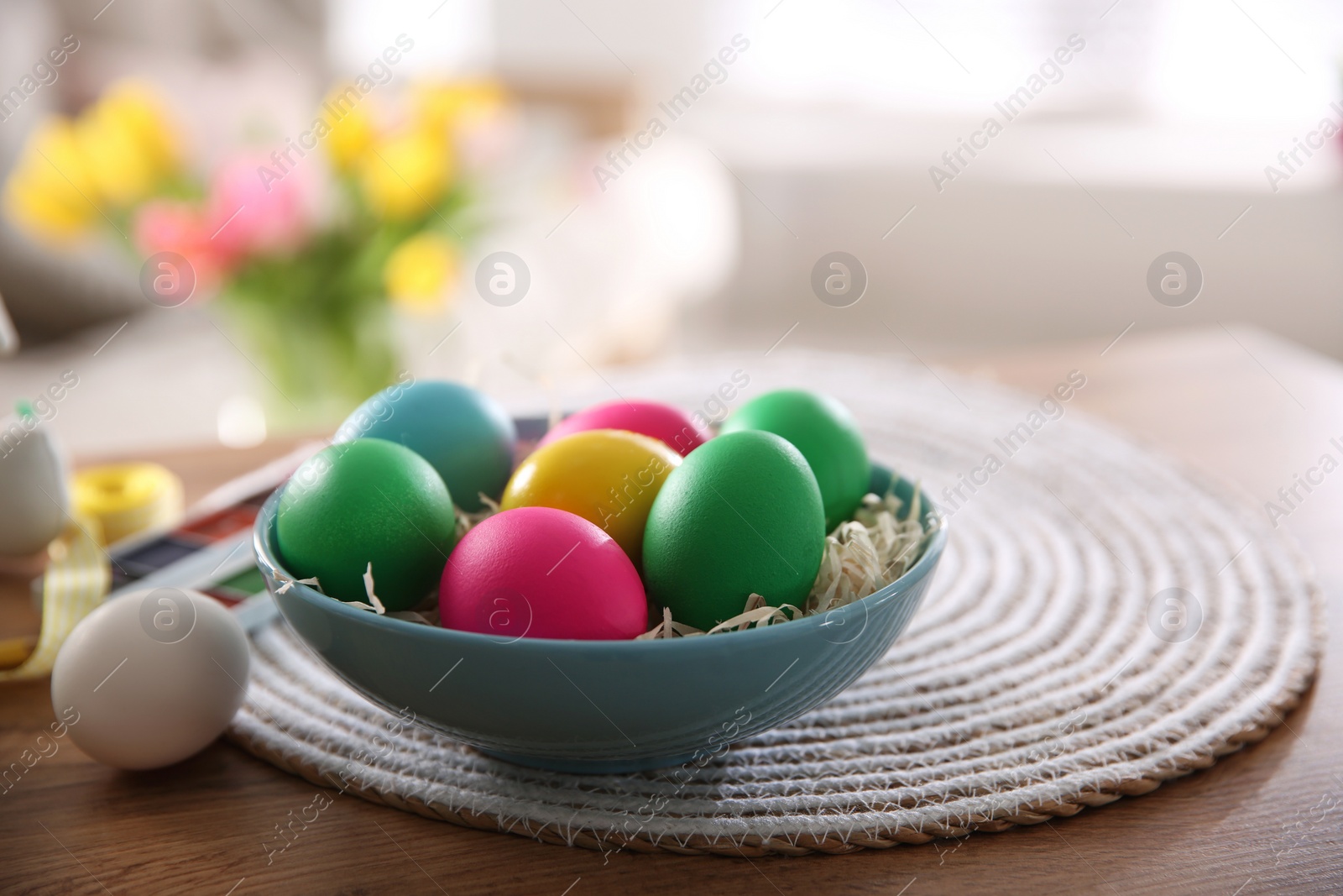 Photo of Bright painted Easter eggs in bowl on wooden table indoors, space for text