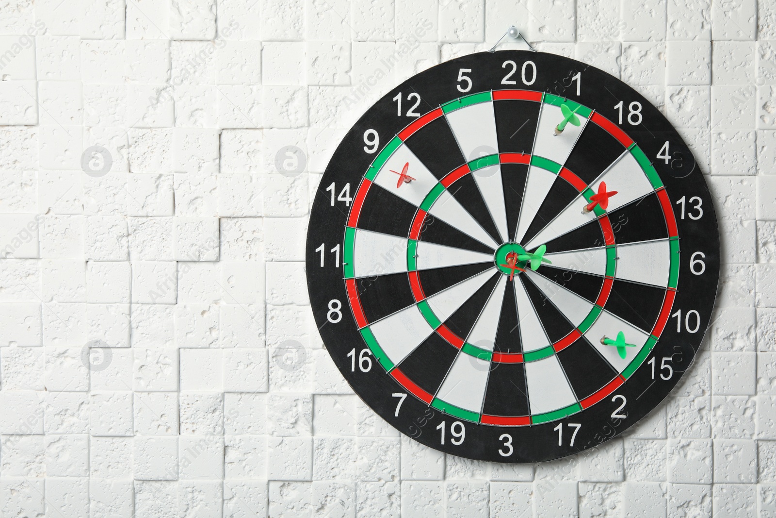 Photo of Arrows hitting dart board on white textured wall. Space for text