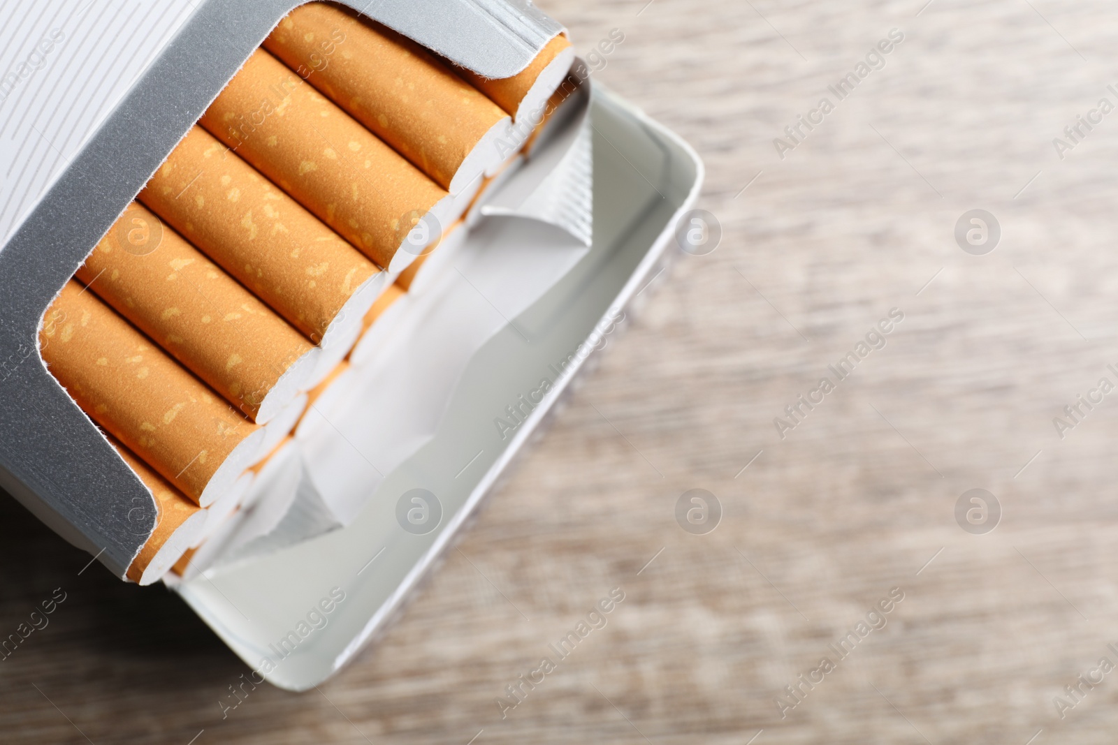 Photo of Cigarettes in pack on wooden table, top view. Space for text