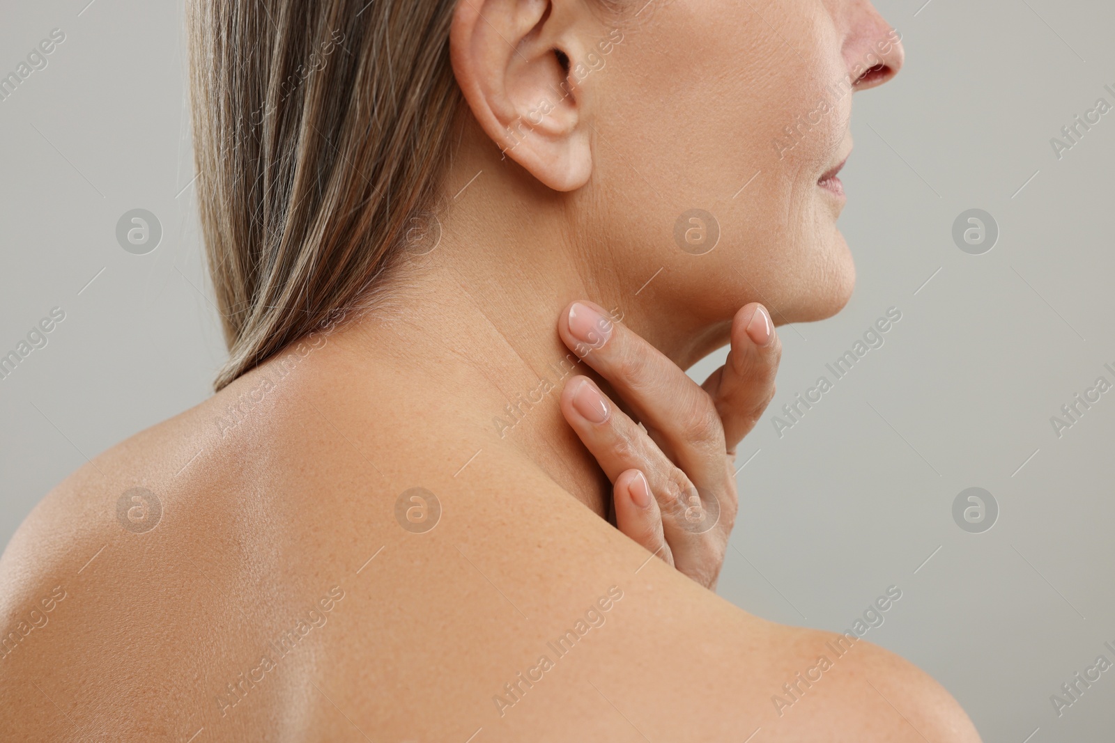 Photo of Mature woman touching her neck on grey background, closeup