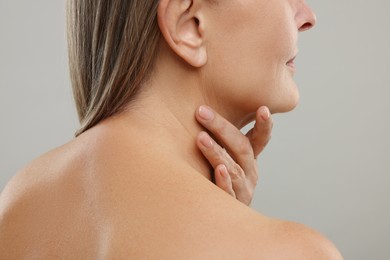 Mature woman touching her neck on grey background, closeup