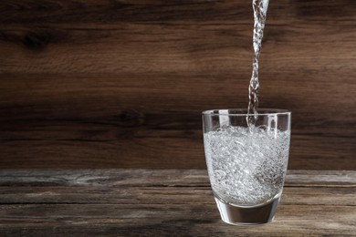 Photo of Pouring soda water into glass on wooden table. Space for text