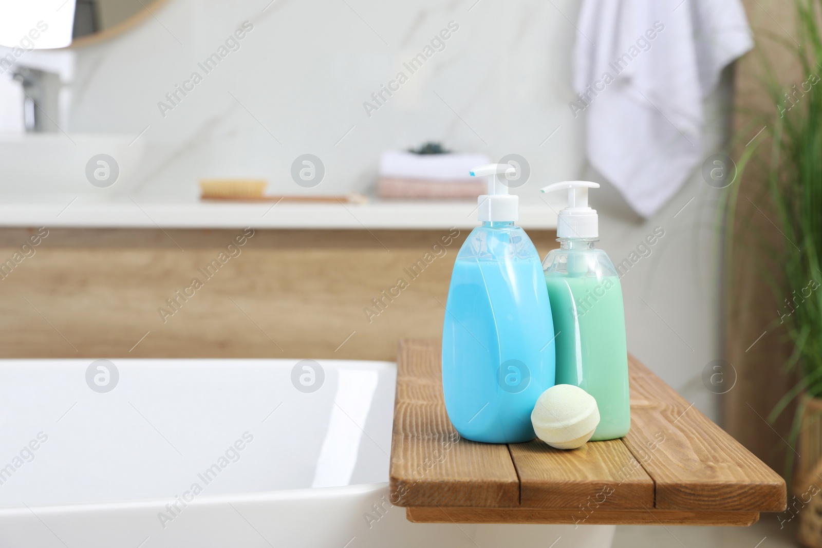 Photo of Wooden tray with bottles of shower gels and bath bomb on tub indoors, space for text